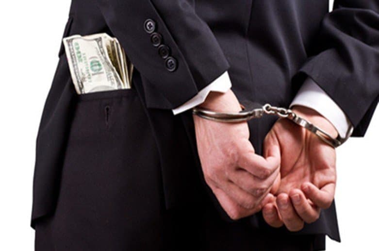A businessman in a suit with handcuffed hands and cash in his pocket