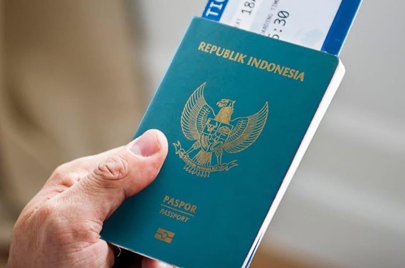 A hand holding an Indonesian passport with a boarding pass tucked inside
