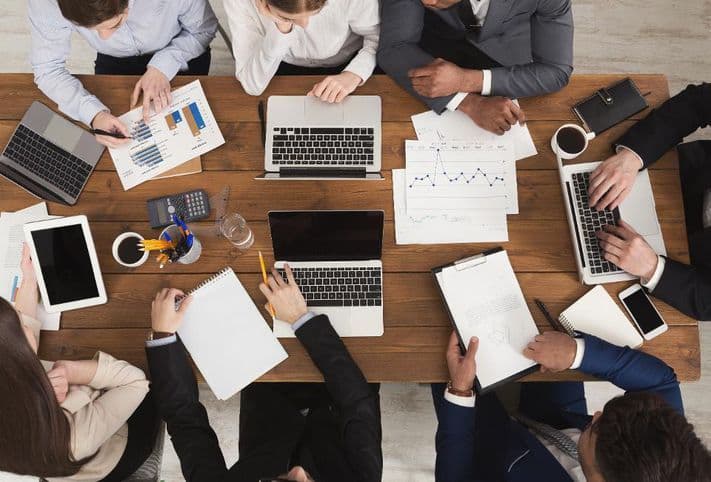 A business team reviewing charts and reports around a table full of laptops